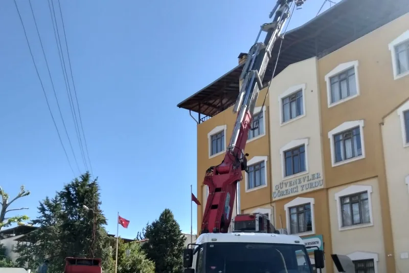 Vinçli kamyonun bomu, dört katlı binanın çatı hizasına uzanmış; sokakta enerji hattı geçiyor.
