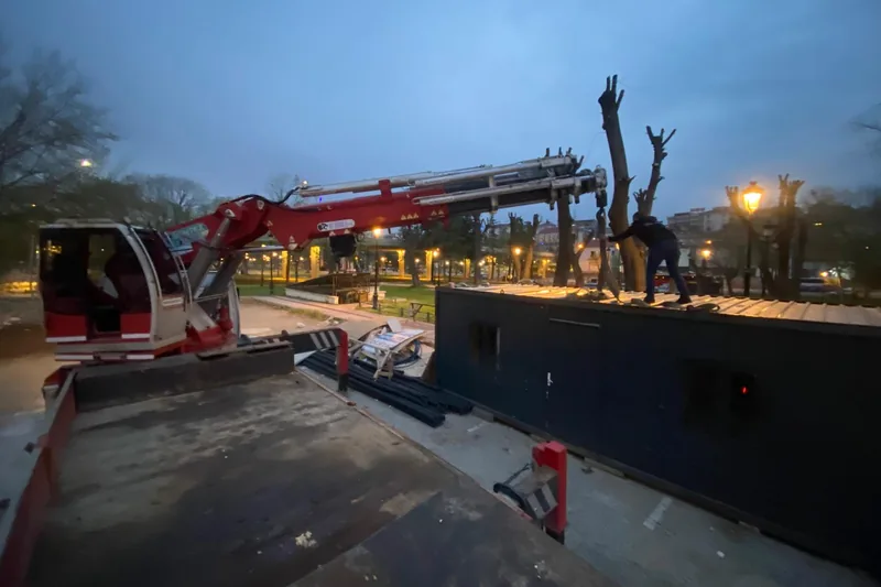Alacakaranlıkta parka indirilen konteyner; bir kişi çatısına çıkmış, kancayı çözüyor.